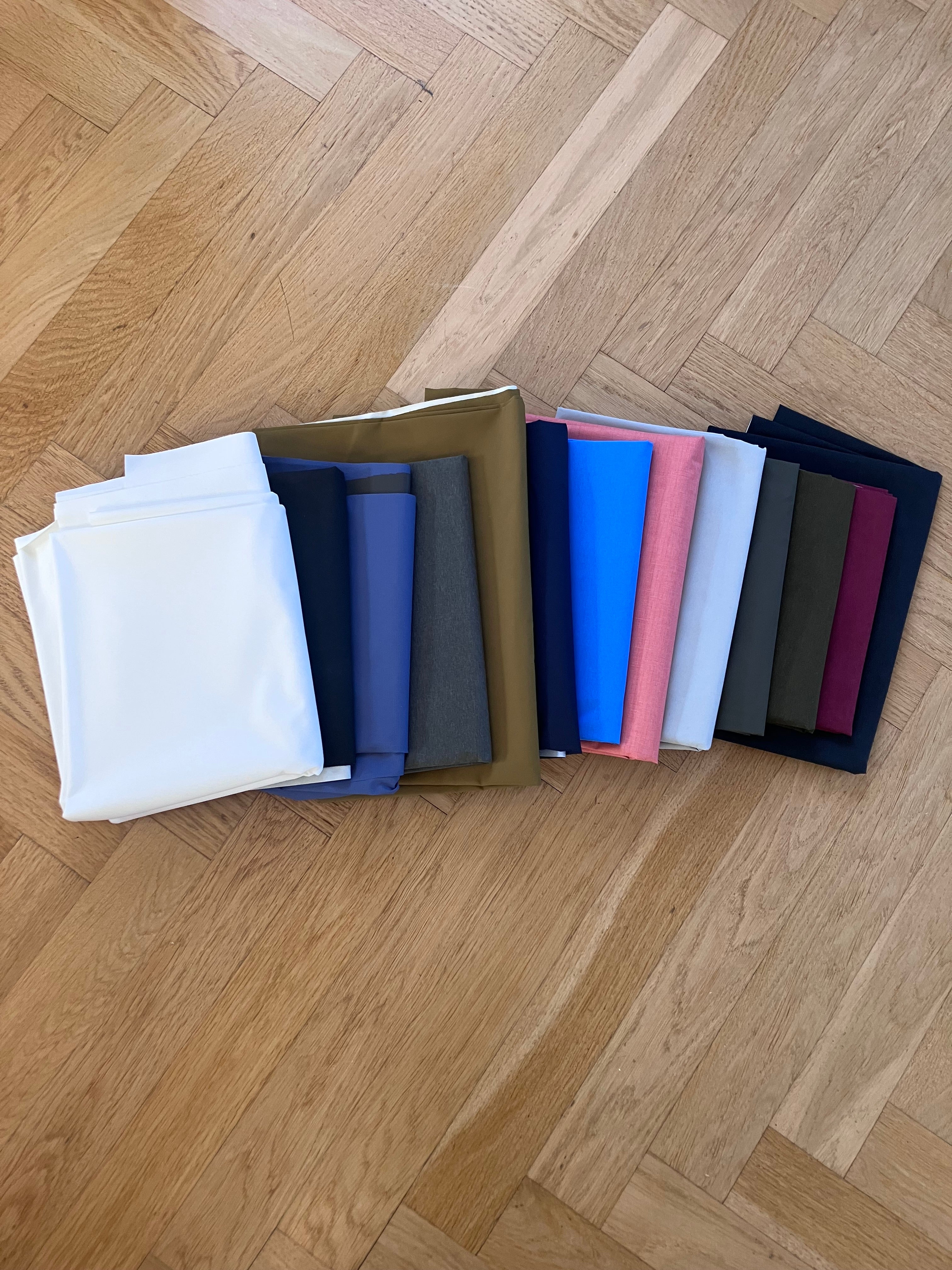 Set of folded fabric swatches in various colors on a wooden floor